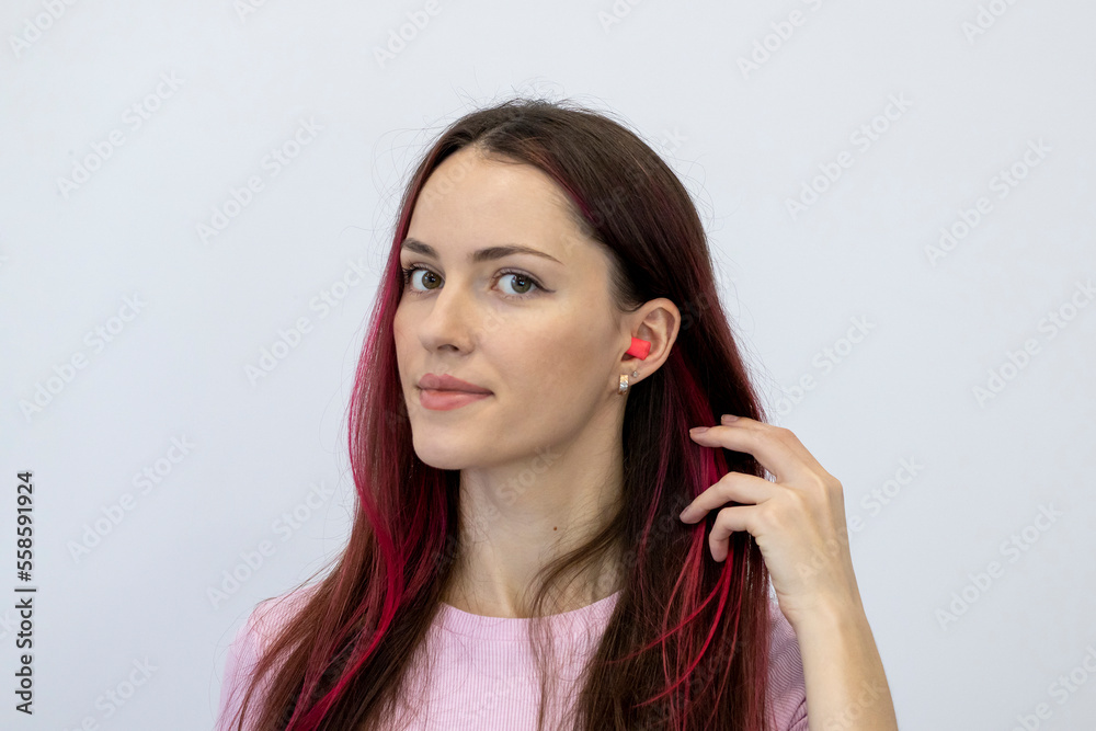 Beautiful young woman with bright pink hair in a pink T-shirt shows her ear with earplugs. Portrait of a woman looking into the camera. Beautiful young woman with bright pink hair in a pink T-shirt shows her ear with earplugs. Portrait of a woman looking into the camera.