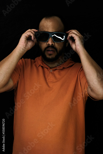 Bearded adult man portrait with ring light and black backdrop with oversized shaded glasses © Spenelo