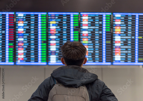 a young man with a backpack is near a flight schedule in the airport