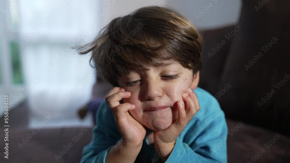 One upset small boy grimacing with hand in chin laying on couch at home One upset small boy grimacing with hand in chin laying on couch at home
