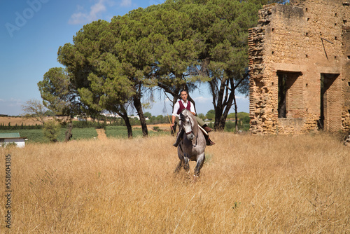 Woman horsewoman, young and beautiful, performing cowgirl dressage exercises with her horse, in the countryside next to a ruined building. Concept horse riding, animals, dressage, horsewoman, cowgirl. © Manuel