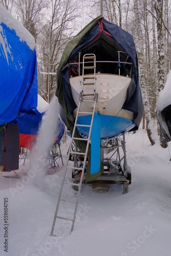 A yacht covered with an awning for the winter, from which snow is removed