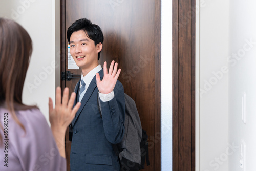 出勤する夫と玄関で見送る妻（夫婦・カップル・行ってらっしゃい・バイバイ）