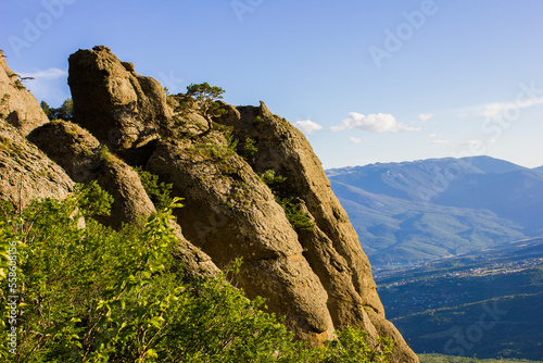 The slope of Demerdzhi Mountain with stones and large boulders covered with trees,with distant hills in a haze and villages in a valley in the summer in Crimea in Ukraine at sunset
