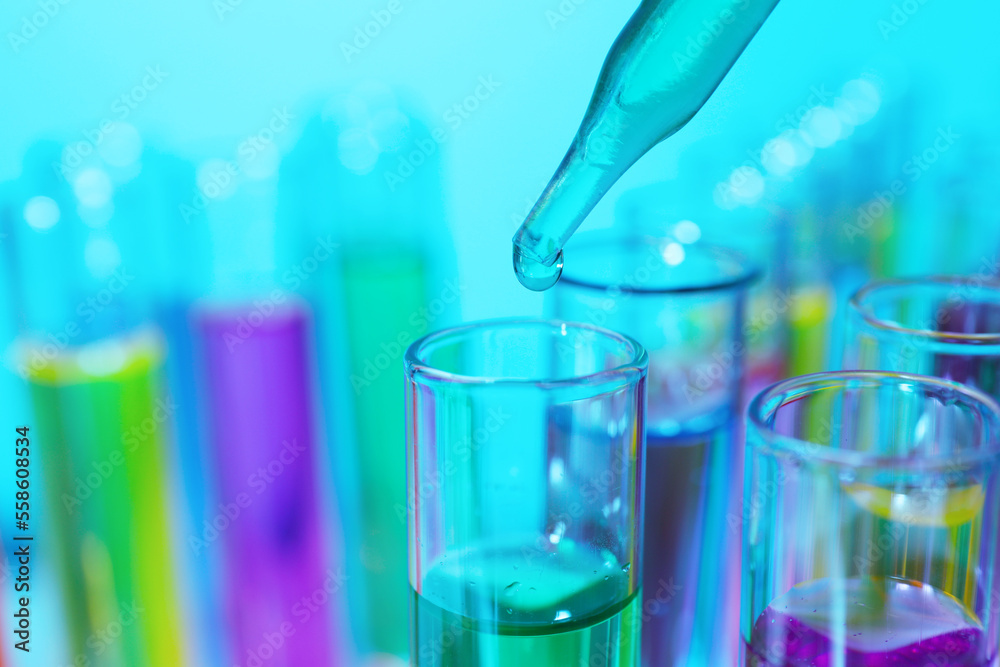Dripping liquid from pipette into test tube on light blue background, closeup Dripping liquid from pipette into test tube on light blue background, closeup