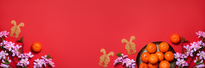 Chinese or lunar new year flat lay with plate of mandarins, paper rabbits as symbol of 2023 and flowers on red