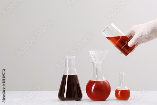 Wallpaper Mural Scientist pouring liquid from beaker into round bottom flask on white table against light background, closeup. Space for text Torontodigital.ca
