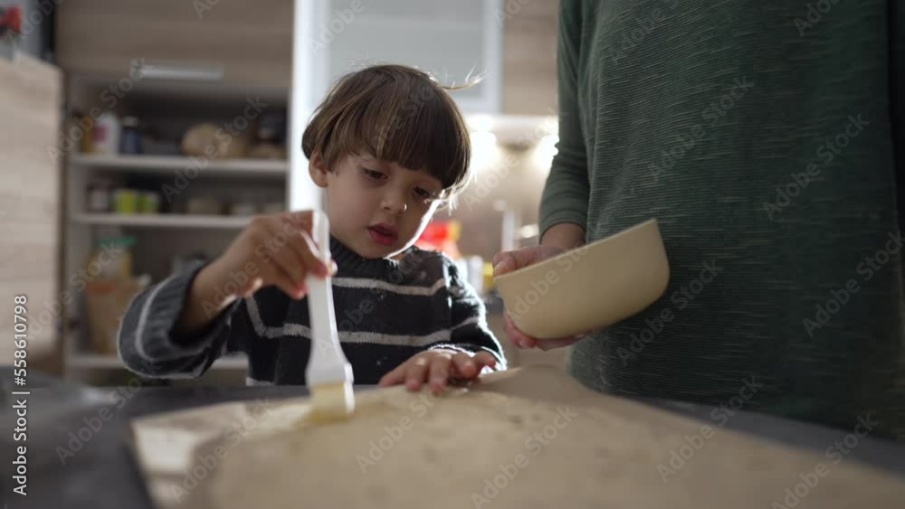 Little boy baking together with mom. Child using baking brush. Mother spending time with son during weekend family activity Little boy baking together with mom. Child using baking brush. Mother spending time with son during weekend family activity