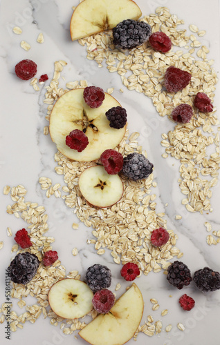 healthy tasty hearty high-calorie oatmeal with fruits and raspberries and blackberries and apples on a white kitchen board. for screensavers signboards labels banners flyers menus