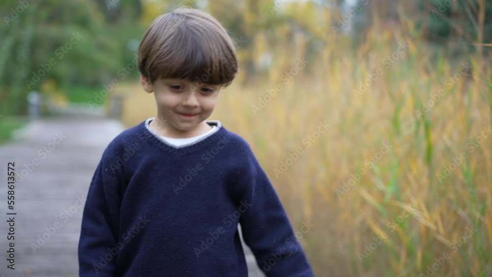 One adorable turning head looking at camera smiling. Portrait of a cute happy small boy walking outside in nature One adorable turning head looking at camera smiling. Portrait of a cute happy small boy walking outside in nature