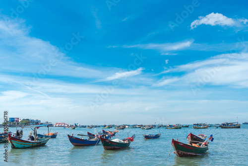 Fleet of small traditional wooden fishing boats anchored near shoreline of Bai Truoc Beach with downtown buildings in distance background at Vung Tau, Vietnam