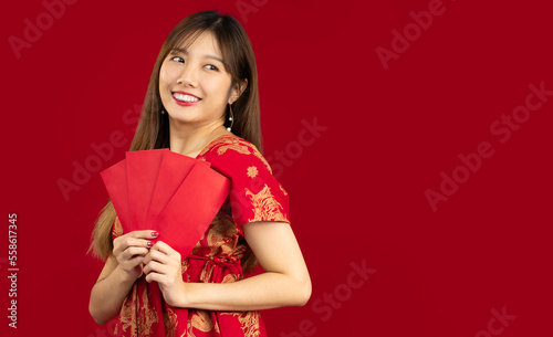 Young beautiful asian woman in red dress holding and showing red envelopes of Chinese New Year bunus and gift on red background.