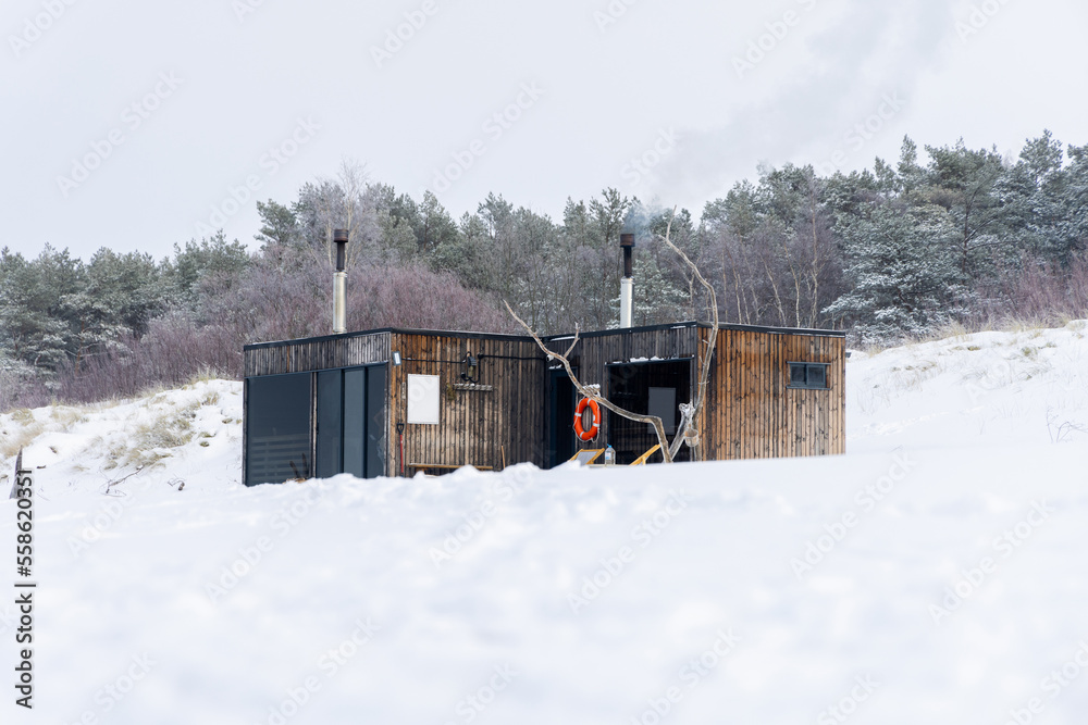 Wooden outdoor sauna with a smoke coming out of chimney on a beautiful cold snowy winter day at the Baltic sea. Well being and healthy life style.
