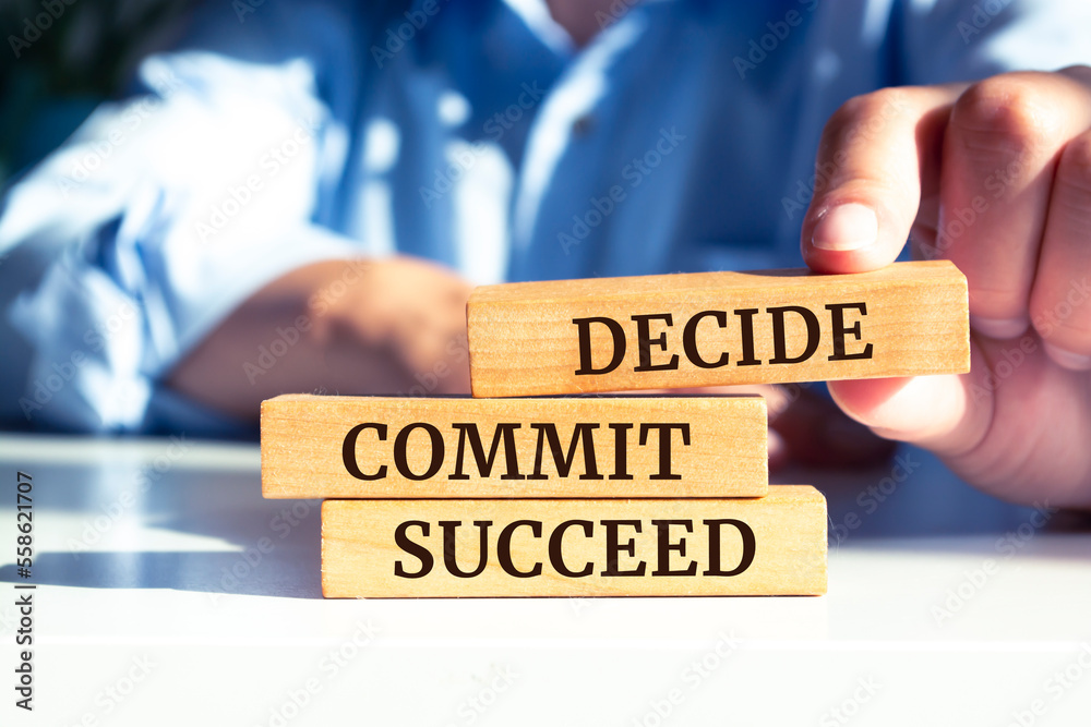 Closeup on businessman holding a wooden blocks with text 'DECIDE COMMIT SUCCEED', business concept Closeup on businessman holding a wooden blocks with text 'DECIDE COMMIT SUCCEED', business concept
