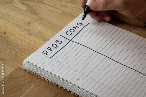 Fotografie A man writes a list of pros and cons by hand in a notepad on a desk in order to