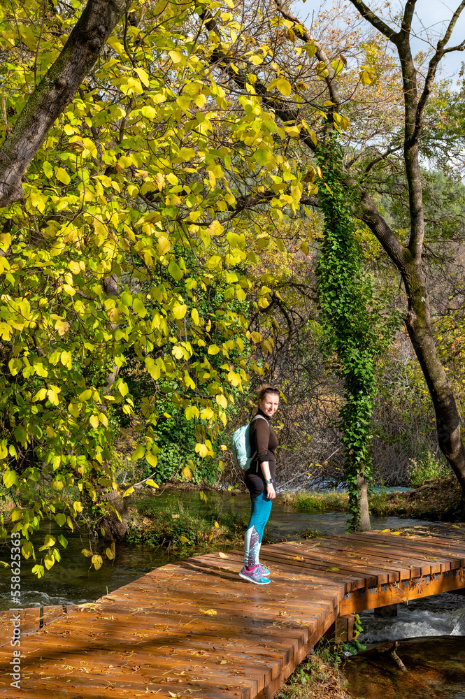 Obraz premium Woman walking in Krka National Park during colorful autumn travel destination in Dalmatia, Croatia, Europe. Female and fall colors leafs on trees. Krka Waterfalls and water in sunny morning light fog.