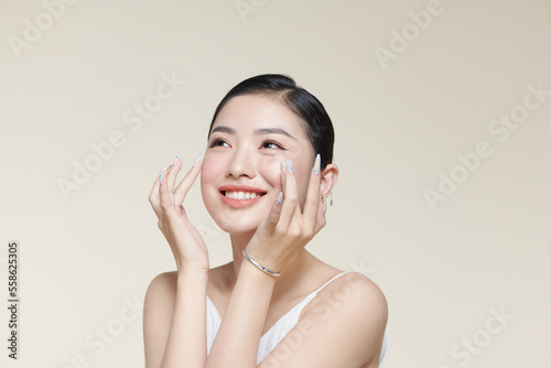 Beautiful young woman with clean fresh skin touching her face