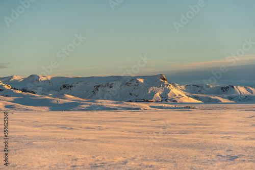 montañas de tierra volcánica nevadas, rodeadas de campos de nieve con el cielo azul claro e iluminadas por las primeras luces del día