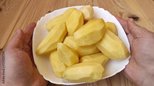 A man holds a plate of peeled raw potatoes in his hands. Potato without skin. Cooking concept.