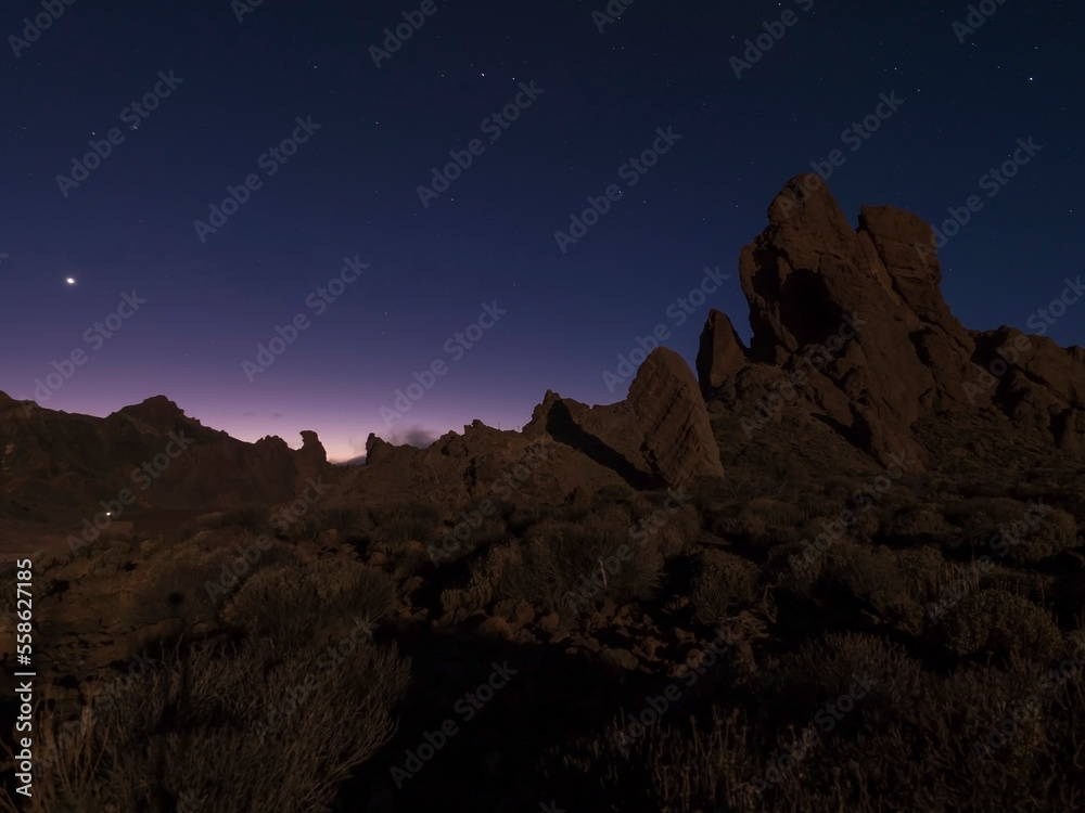 Long exposure night shot of Roques de Garcia volcanic rock formation at El Teide national park, early night winter sky with stars on pink blue glow. Tenerife Canary islands, Spain