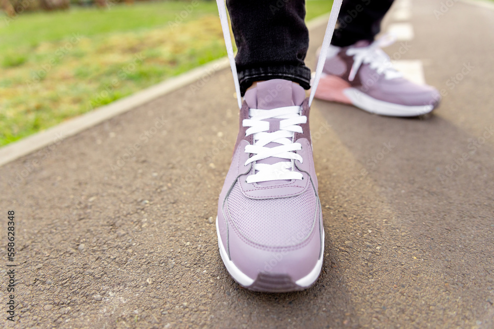 woman in sneakers stands on path and ties her shoelaces. Womens legs in pink sneakers close up