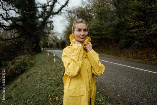Pretty woman in yellow raincoat walking in rainy weather in the countryside