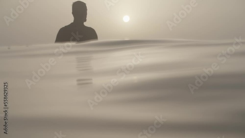 Unrecognizable Surfer silhouette sitting on Surfboad wainting for the swell, Mystic atmosphere in Slow motion photo