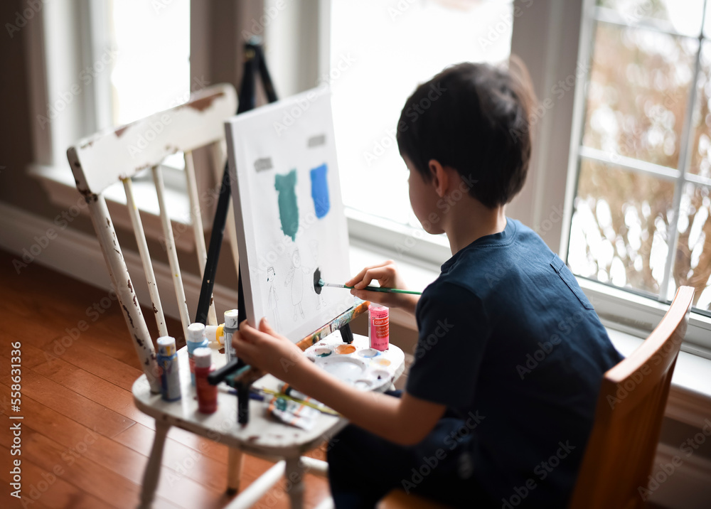 Young boy painting on a canvas on an easel in front of a window. Young boy painting on a canvas on an easel in front of a window.