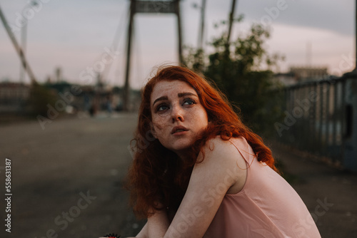 Portrait of teenage girl with freckles sitting on bridge in city photo