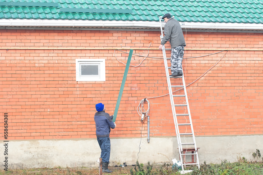 two men prepare their house for a snowy winter, they install snow traps ...