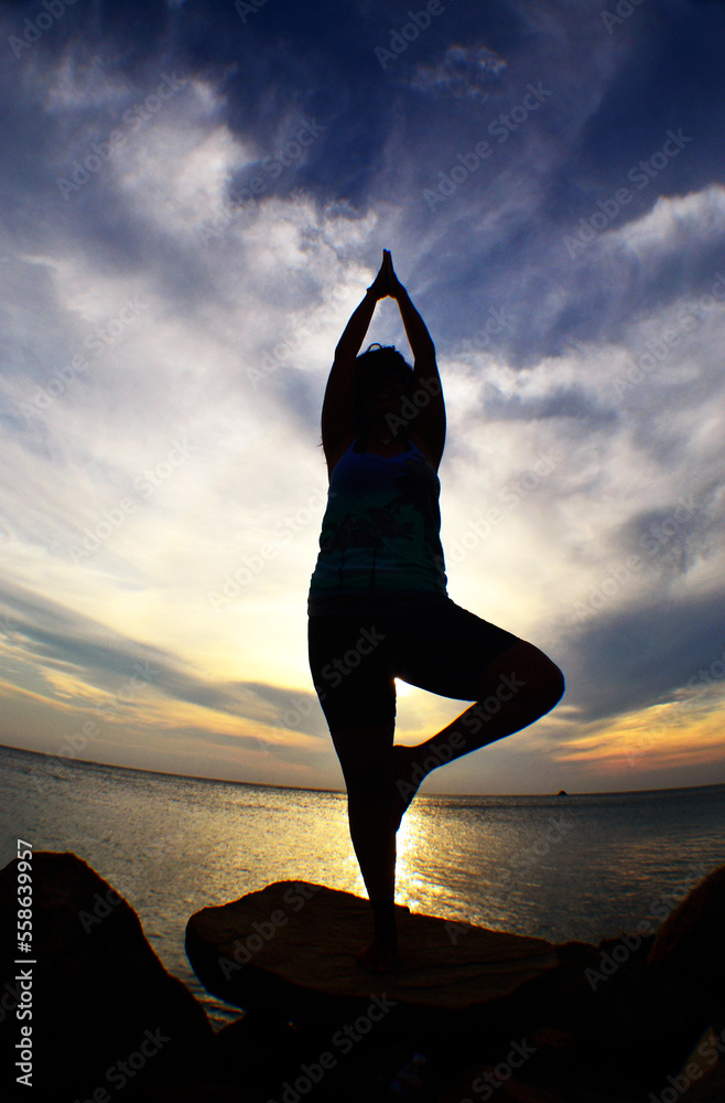 a woman doing the yoga position in a sunset at the sea
