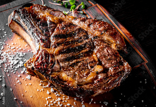 Fotografie Grilled Ribeye Steak on bones on wooden board, prime cowboy steak on dark backgr