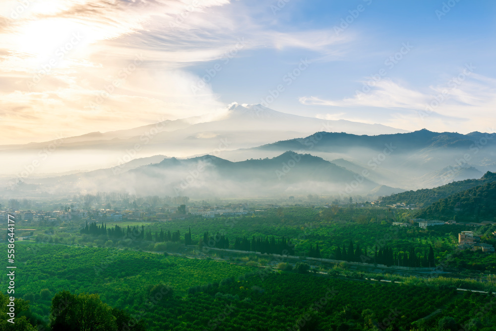 view at beautiful misty spring mountain valley with green gardens and mountains in mist on background of landscape