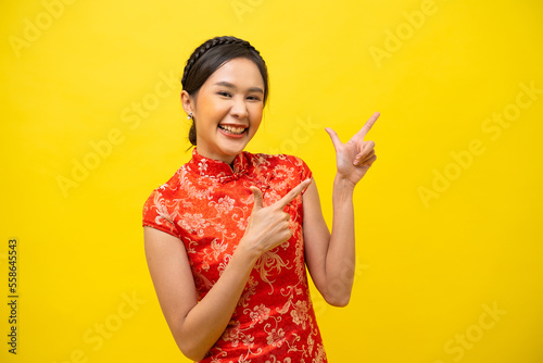 Fotografie Beautiful Asian woman wearing traditional cheongsam with hand pointing up to copy space isolated on yellow background, Happy Chinese New Year