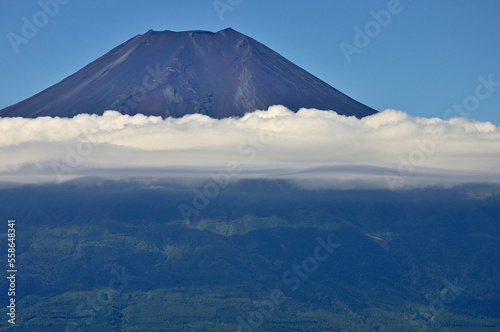 道志山塊の杓子山山頂より望む夏の富士山 杓子山は道志山塊の西に聳える山。富士吉田市と都留市、そして忍野村との行政界に位置する山。遠方から杓子山方面を眺めると富士山に近いこともありすぐにそれと分かるが、そのときに最も標高が高い山容は鹿留山或いは子ノ神であり、その隣のやや低い場所の山が杓子山になる。山梨百名山である杓子山の山頂からは、天候に恵まれれば四囲に視界を遮る樹木はほとんどないことから360度の