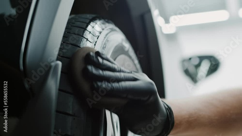 Employee working at the car wash. Close up of male hands with gloves using detailing wax cream for tire wash the car