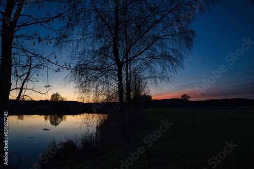Wonderful blue golden red sky after sunset with trees in foreground at a lake with its reflections 