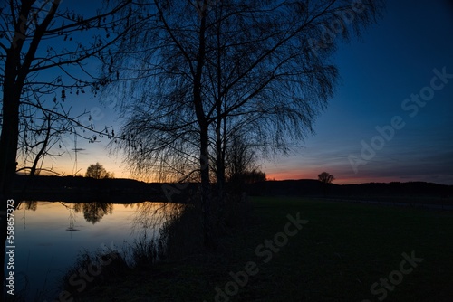 Fototapeta Naklejka Na Ścianę i Meble -  Wonderful blue golden red sky after sunset with trees in foreground at a lake with its reflections 
