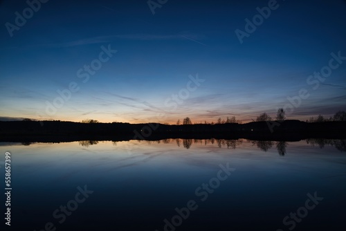 Wonderful blue golden red sky after sunset with trees in foreground at a lake with its reflections 