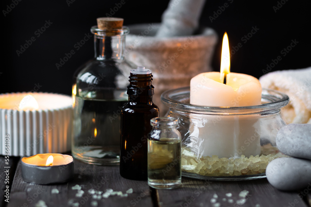 Spa setting with essential oil, candle, sea salt, pebbles, towel on dark wooden background. Massage, aromatherapy. Natural organic ingredients for relaxation, detention. Wellness in salon concept Spa setting with essential oil, candle, sea salt, pebbles, towel on dark wooden background. Massage, aromatherapy. Natural organic ingredients for relaxation, detention. Wellness in salon concept