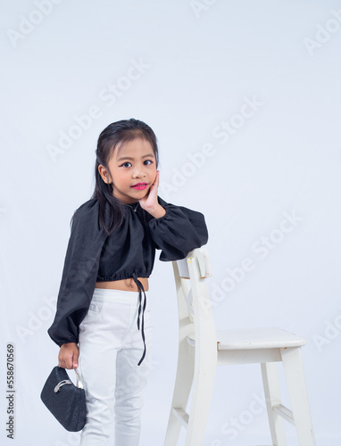 Fashinable little cute girl holding a black handbad in style as she poses in studio on white background isolation. 
