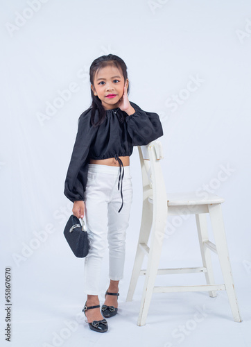 Fashinable little cute girl holding a black handbad in style as she poses in studio on white background isolation. 