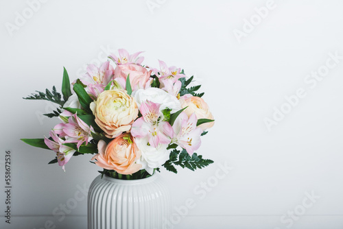 Beautiful bouquet of fresh colorful pastel ranunculus and lily flowers in full bloom with green fern leaves in vase against white background, close up. Negative space.