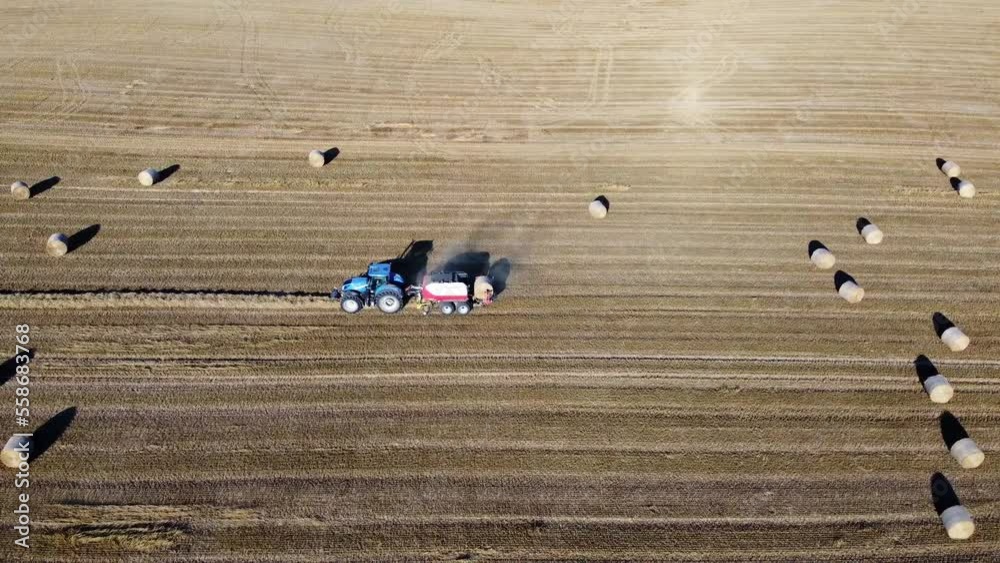 Tracteur en train de faire des bottes de foin. Vue de profil avec le tracteur munis de sa presse à foin qui fait tomber une boule.
