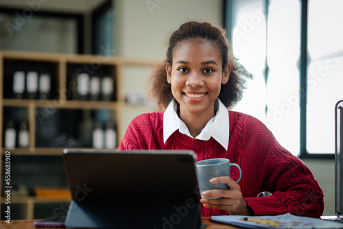 American teenage woman sitting in office with laptop, she is a student studying online with laptop at home, university student studying online, online web education concept.