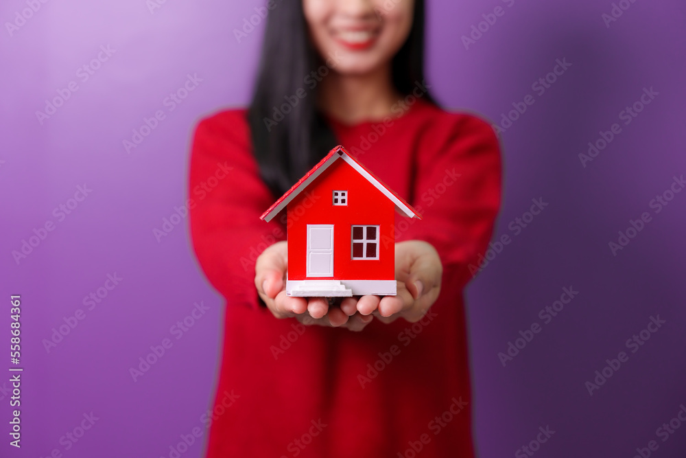 Portrait of beautiful trendy asia cheerful girl holding home toy model showing copy space ad isolated over violet color background, for valentine day color tone Portrait of beautiful trendy asia cheerful girl holding home toy model showing copy space ad isolated over violet color background, for valentine day color tone