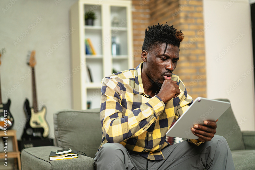 Cheerful young man paying bills online with credit card and digital tablet. African man using credit card at home. Cheerful young man paying bills online with credit card and digital tablet. African man using credit card at home.