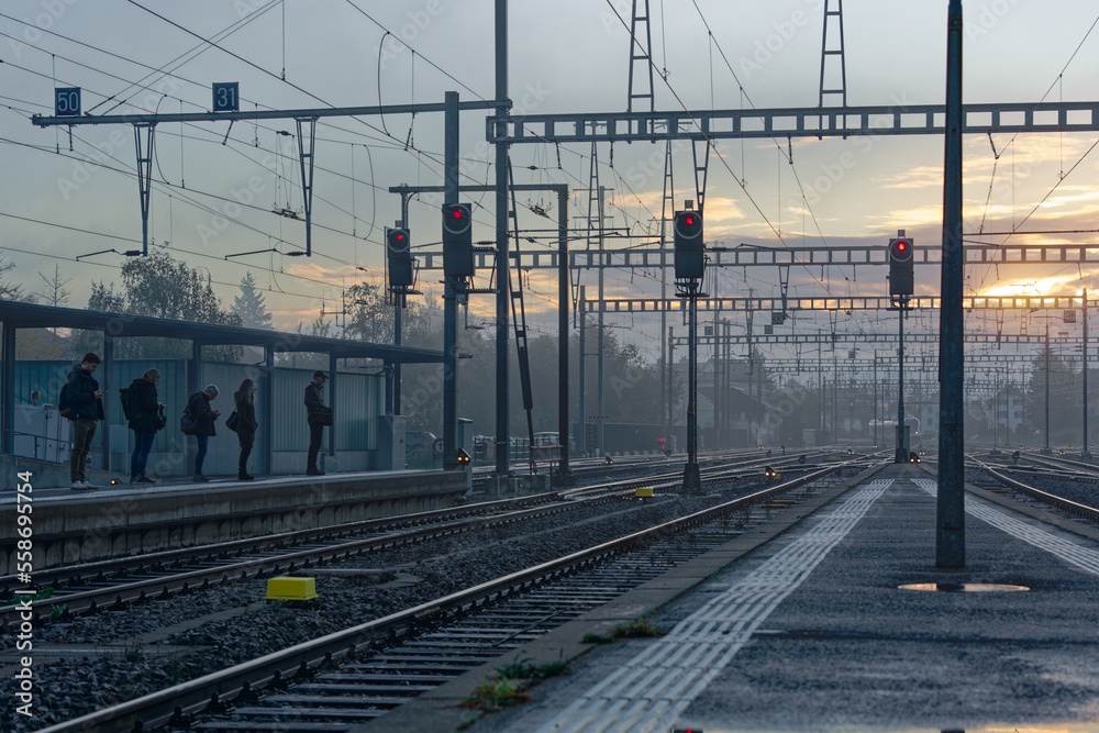 Commuters waiting at railroad platform at railway station of Swiss City Biel Bienne on a sunny foggy autumn morning. Photo taken November 10th, 2022, Biel Bienne, Switzerland. - obrazy, fototapety, plakaty 