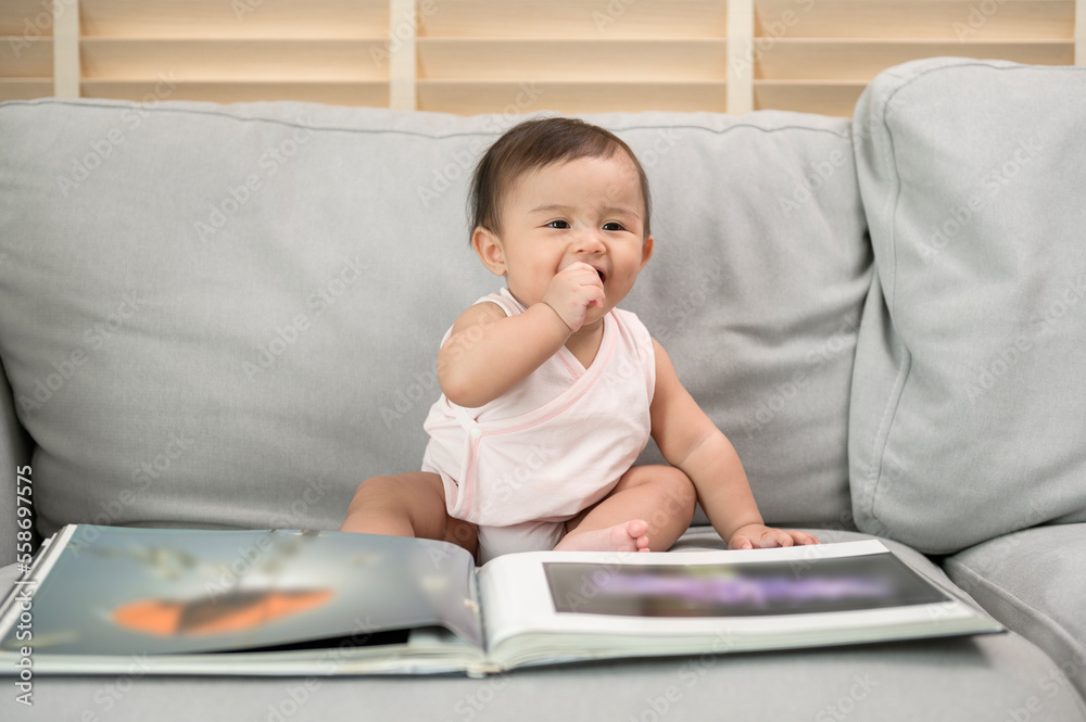 Baby girl reading a book sitting on sofa at home Baby girl reading a book sitting on sofa at home