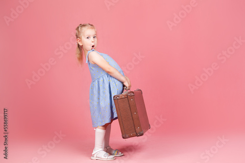 a little surprised girl on a pink background with a suitcase in her hands